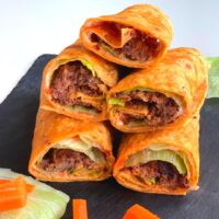 Kidney Bean Patties Wraps arranged on a black cheese board with some carrots and lettuce seen on the side.