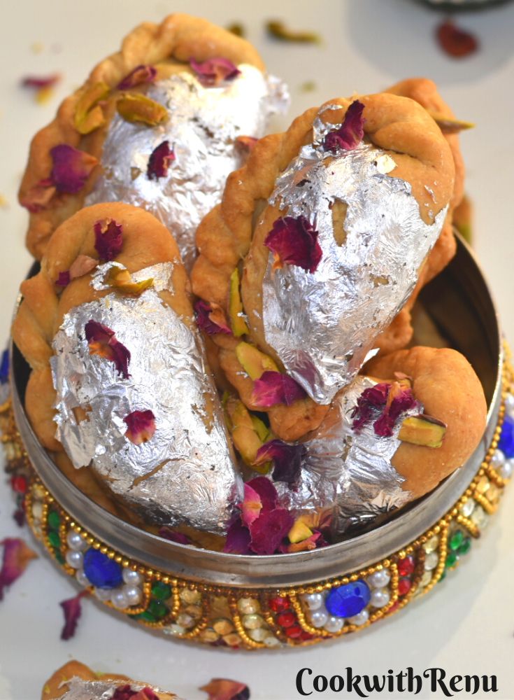 Close up look of Air Fryer Mawa Gujiya presented in a designer colourful bowl. Gujiyas are garnished with edible silver leaves, rose petals and chopped pistachio.