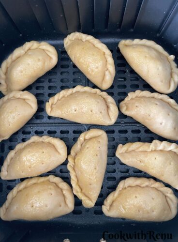 Gujiya getting ready to be baked in Air Fryer with a coating of ghee all over.