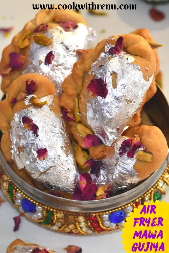 Close up look of Air Fryer Mawa Gujiya presented in a designer colorful bowl. Gujiyas are garnished with edible silver leaves, rose petals and chopped pistachio.