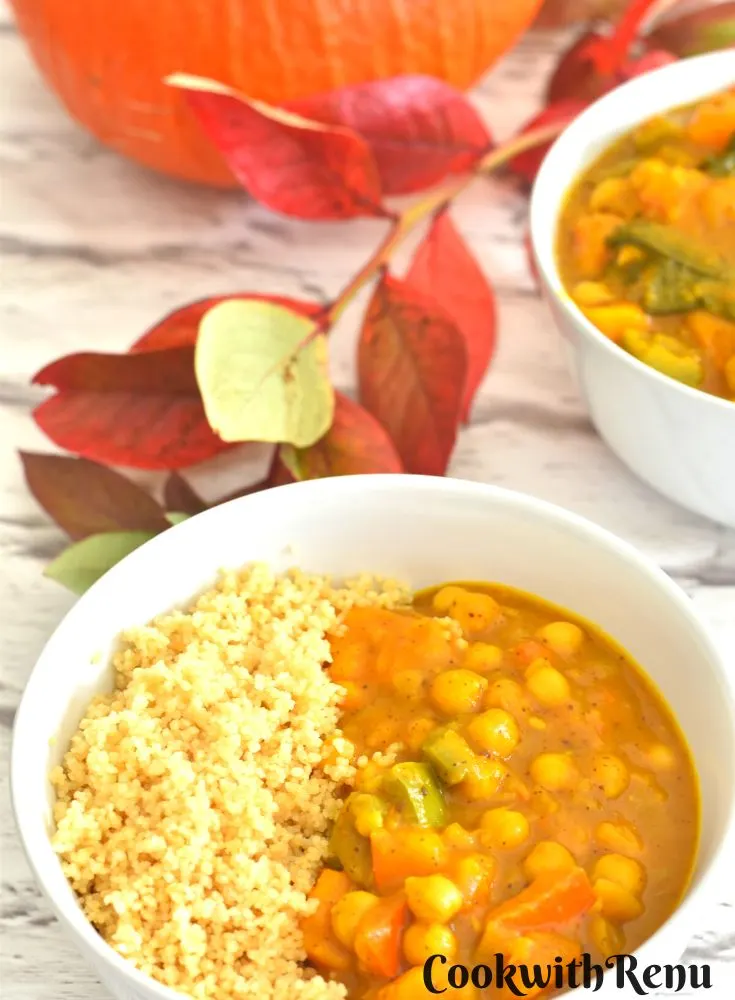 Uchiki Kuri Pumpkin Chickpea Kale Curry served along with cooked couscous in a white bowl, seen in the background is pumpkin and some fall leaves.