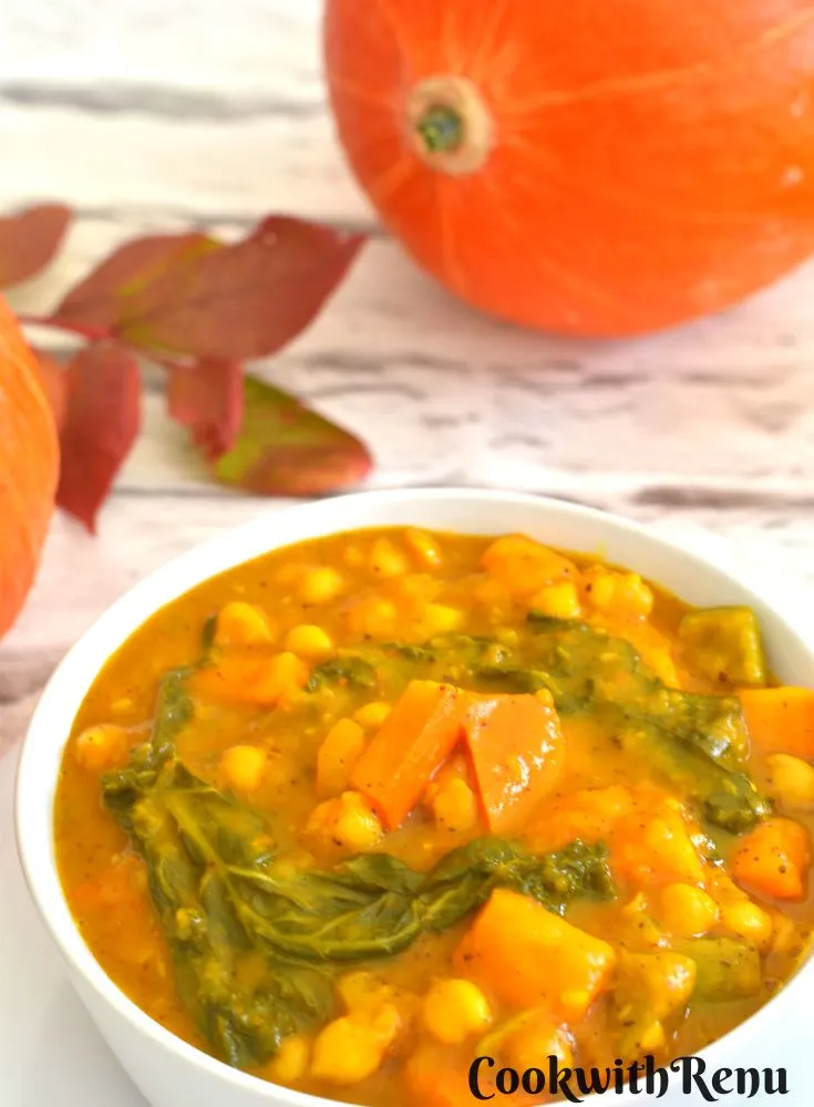 Red Uchiki Kuri pumpkin garbanzo beans vegan Curry served in a white bowl, seen in the background is pumpkin and some fall leaves.
