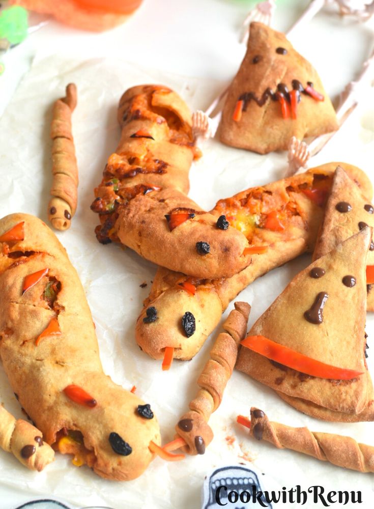 Halloween Stuffed Snake bread , witch hat and mini snake breadsticks arranged on a white parchment paper, with some festive decorations seen on the side.
