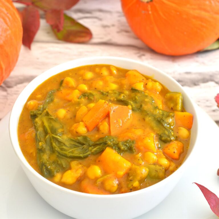 Uchiki Kuri Pumpkin Chickpea Kale Curry served in a white bowl, seen in the background is pumpkin and some fall leaves.