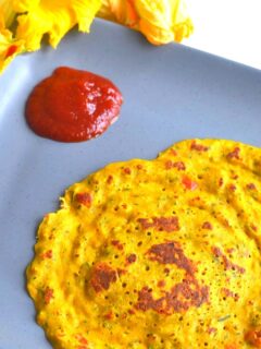 Zucchini and Squash Blossom Pancakes in grey plate with tomato ketchup and seen are some squash flowers.