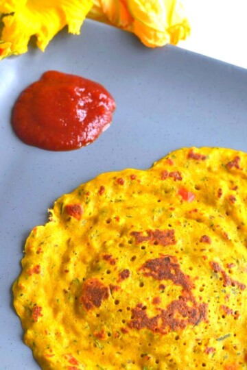 Zucchini and Squash Blossom Pancakes in grey plate with tomato ketchup and seen are some squash flowers.