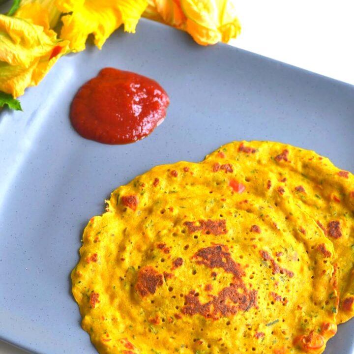 Zucchini and Squash Blossom Pancakes in grey plate with tomato ketchup and seen are some squash flowers.