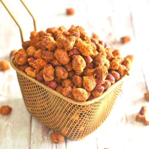 Air Fryer Masala Peanuts in a golden brown colander, with some peanuts scattered around.
