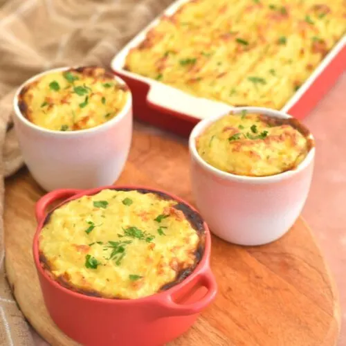 Air Fryer Shepherdless Pie in individual ramekin molds in front on a brown cheese board and seen behind in a rectangular dish.