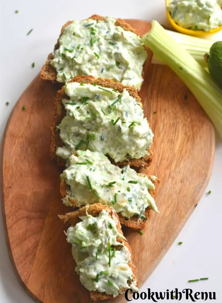 Open Face Avocado Celery Sandwich served on a brown cheese board with a garnish of chives. Seen along side are some celery sticks and avocado.
