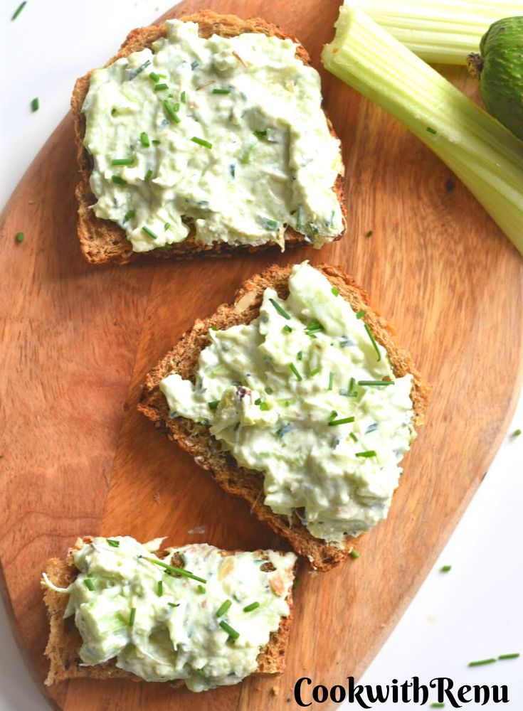 Top view of Open Face Avocado Celery Sandwich served on a brown cheese board with a garnish of chives. Seen along side are some celery sticks and avocado.