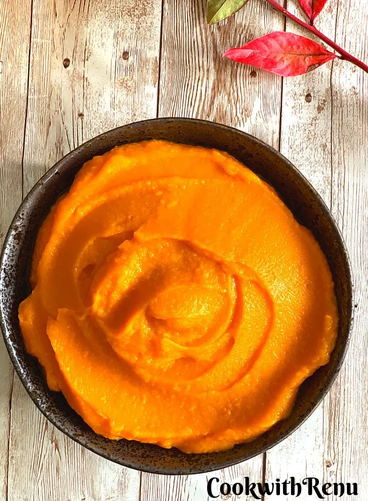 Pumpkin puree in a dark brown bowl, with some autumn leaves in background.