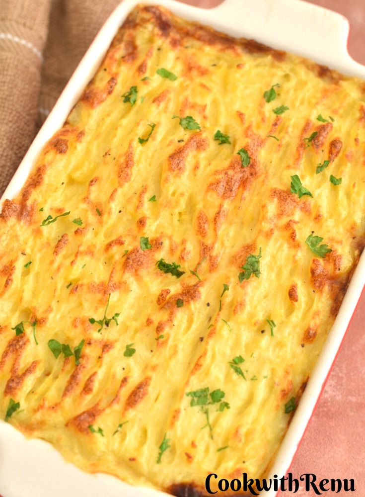 Clouse up look of Vegetarian Shepherds pie in a red rectangular baking tray. Seen in the background is a brown kitchen towel.