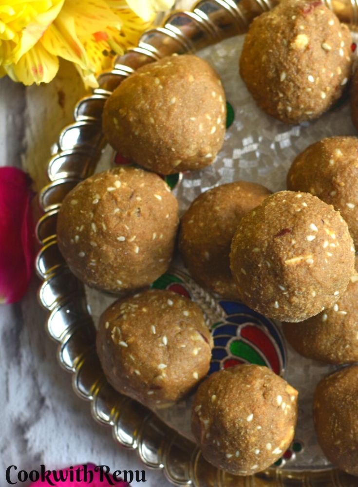 Top view of Gluten-free Bajra ladoo served in a golden tray with some flowers on the side.