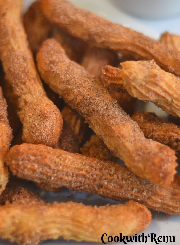 Close up look of Eggless, butterless and baked churros served on a white plate served with some dipping chocolate sauce.