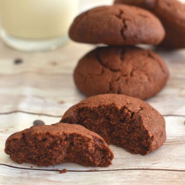 Close up look of a half cut cookie, with more cookeis on a board and a glass of milk.