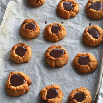 Chocolate Filled Hazelnut Thumbprint Cookies on a baking tray lined with parchment paper.