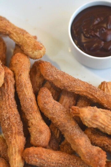 Eggless, butterless and baked churros served on a white plate served with some dipping chocolate sauce.