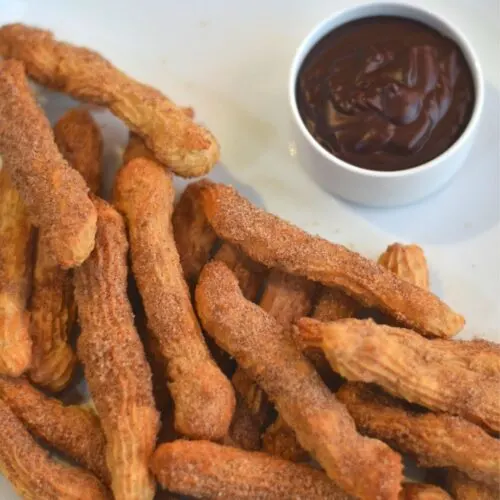 Eggless, butterless and baked churros served on a white plate served with some dipping chocolate sauce.