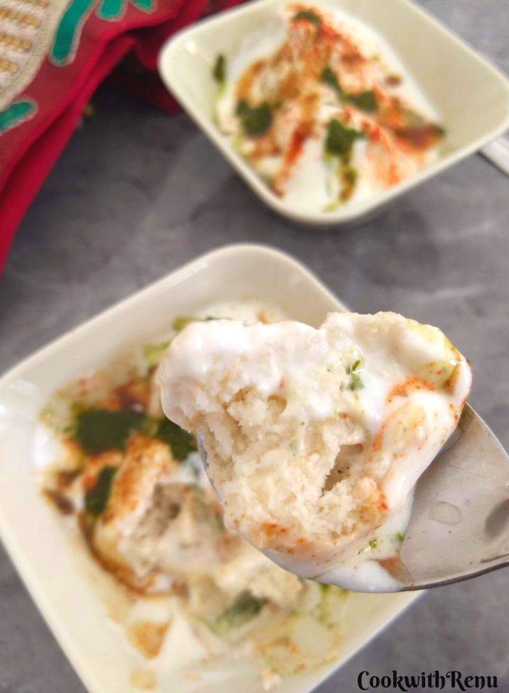 Close up look of dahi bhalla's texture in a spoon, which is topped up with chutneys.
