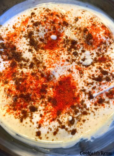 Dahi Bhalla served in large bowl topped up with red chilli powder and cumin powder.