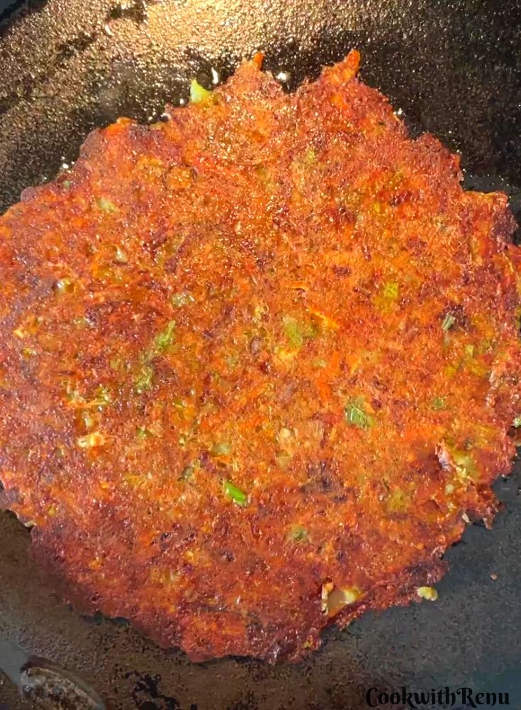 Pearl millet chilla getting cooked on other side on a cast iron pan.