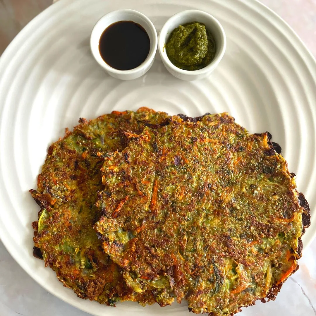 Sprouted Bajra Vegetable Chilla served in a white plate along with tamarind and coriander chutney.