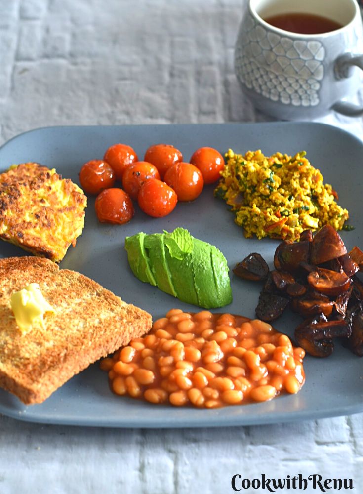 Vegan Irish Breakfast served on a grey plate along with some coffee in a grey cup. The breakfast consist of (anticlockwise from front) baked beans, sauteed mushroom, Indian style tofu bhurji, sauteed tomato, hash browns, butter and in the center avocado.