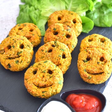 Baked Sweet Potato and Oats patties arranged on a black cheese board with some lettuce in the background and served with some ketchup and cream cheese.