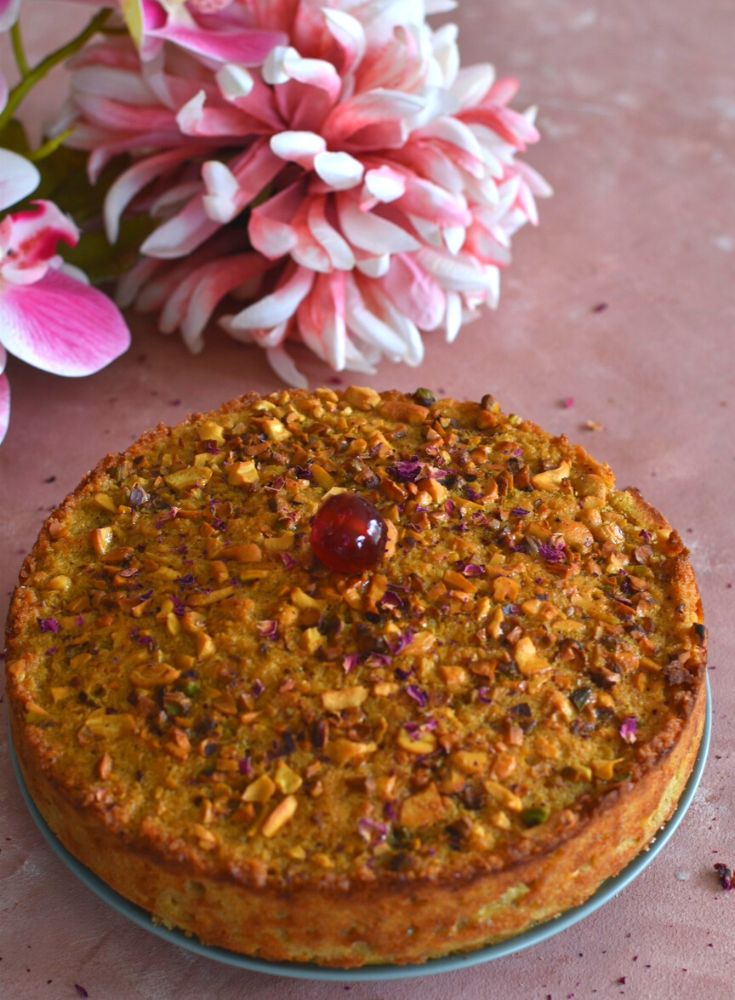A 9-inch round Goan Baath cake is seen with a cherry topping and flowers in the background.