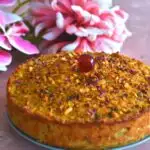 A 9-inch round Goan Baath cake is seen with a cherry topping and flowers in the background.