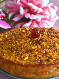 A 9-inch round Goan Baath cake is seen with a cherry topping and flowers in the background.