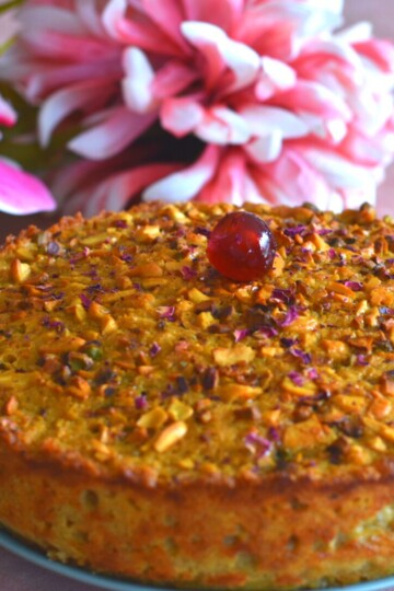 A 9-inch round Goan Baath cake is seen with a cherry topping and flowers in the background.