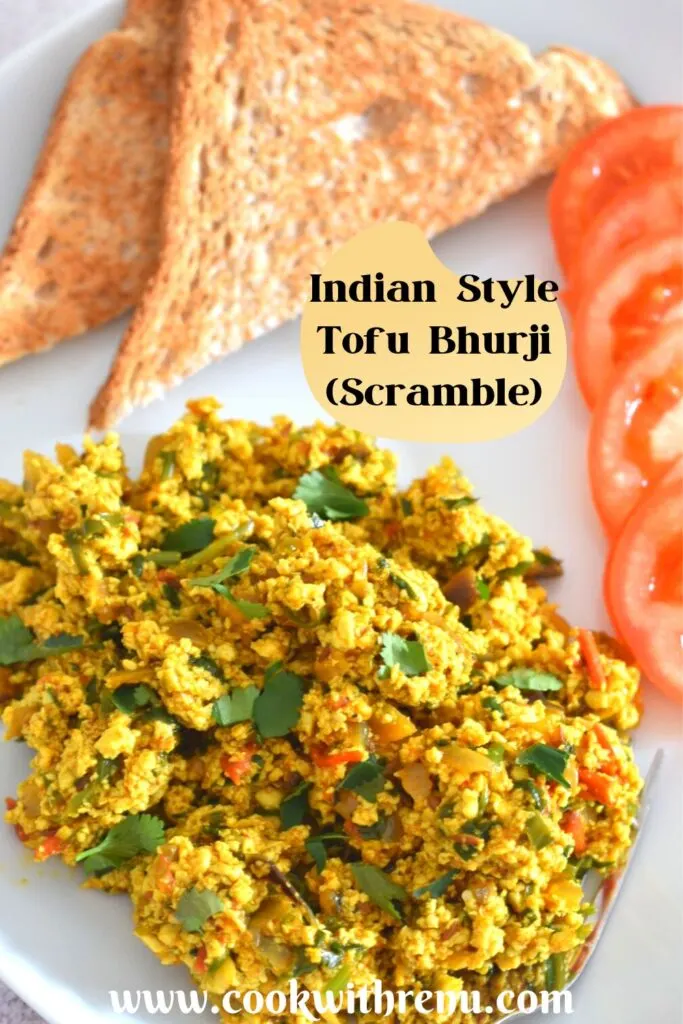 Indian-Style Tofu Scramble served on a white plate with 2 bread slices, few tomato. Seen in the background is a white kettle and a black scarf.