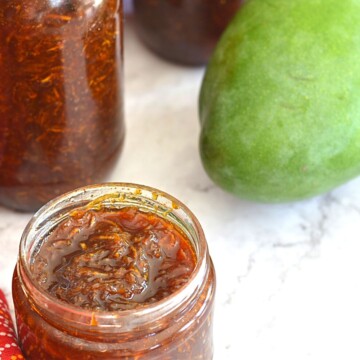 Instant Kairi Gur Chunda in 3 glass jars. There is a raw mango seen on the side.