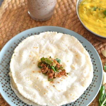 4 Rice bhakris served on a plate with thecha on top and solkadhi and pithla seen in the background.
