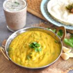 Besan Pithla served in a kadai, with garlic and coriander seen in the side along with a glass of solkadhi and rice bhakri in a plate.