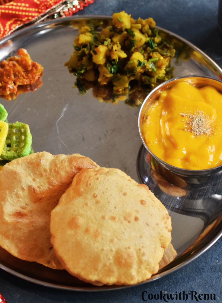 Thali with poori, Aamras , dry potato bhaji, pickle, and fryums.