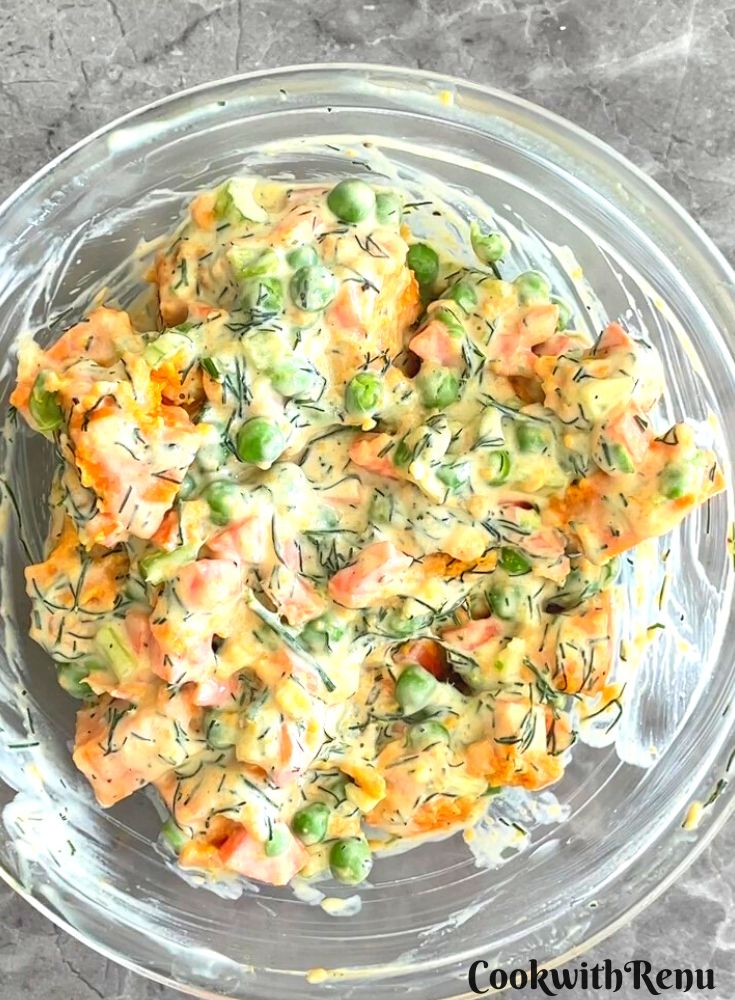 Salad all mixed up along with the dressing in a transparent glass bowl.