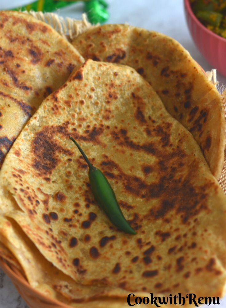 Triangular Ajwain Paratha stacked on a basket, with a green chili on it. Seen in the background is some green capsicums veg