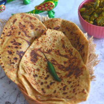 Triangular Ajwain Paratha stacked on a basket, with a green chili on it. Seen in the background is some green capsicums veg