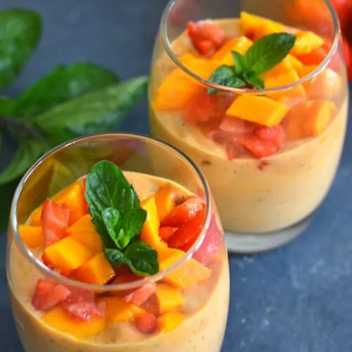 Refreshing Strawberry Mango Chocolate Mint herb Smoothie served in 2 glasses with some mint and strawberries seen in background