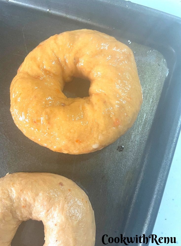 Bagels boiled and ready to be baked arranged in a tray.