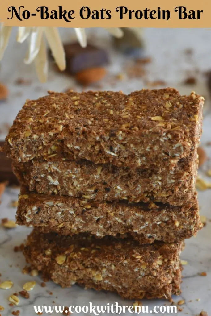 Close up view of No-Bake Oats Chocolate Protein Bar stack one above the other. Seen in the background are some chocolate, almonds and flower.