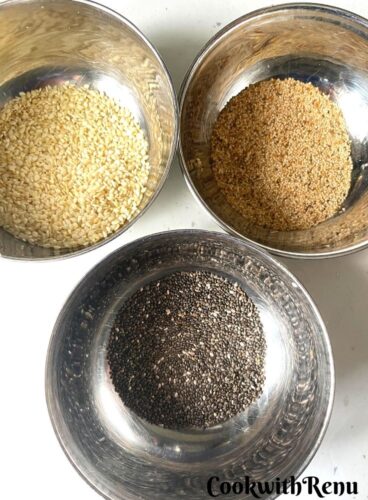 Seeds to be sprinkled on bagels in bowls. There are sesame seeds and poppy seeds.