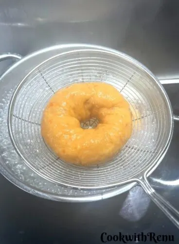 Water Bathing of Bagel done and is seen in a slotted spoon ready to be taken out.