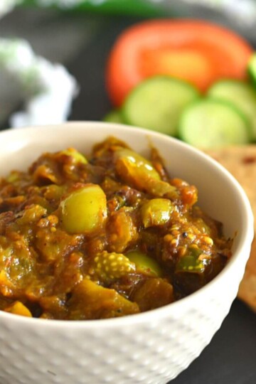 Hare Tamatar ki sabj served in a white bowl with some roti and cucumber tomato salad seen in the background.