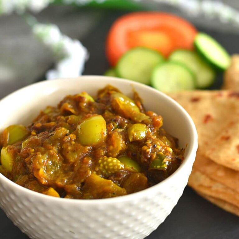 Hare Tamatar ki sabj served in a white bowl with some roti and cucumber tomato salad seen in the background.