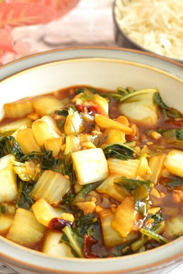 Front and close up view of Bok Choy served in a grey bowl with brown lining. Seen in the background is some white rice.