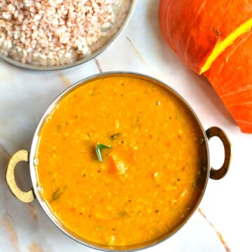 Instant Pot Pumpkin Sambar served in a small kadai/wok. Seen in the background is pumpkin and some red rice.